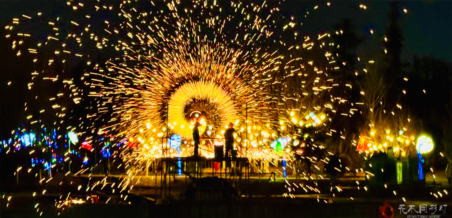 新疆昌吉农业博览园打铁花夜游实景，璀璨的铁花在具有新疆特色的农业建筑上空绽放，游客在丝路主题装置前驻足观赏